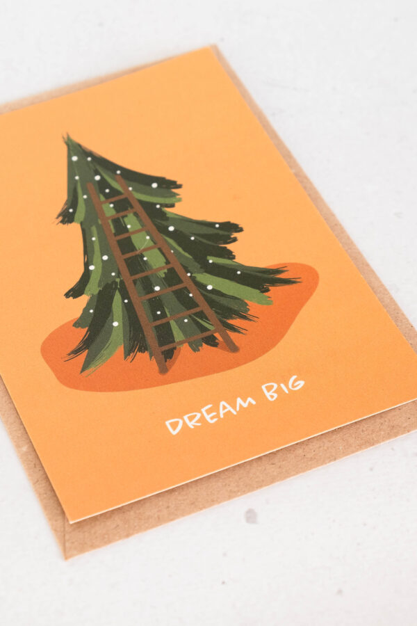 close up kerstkaart uit gerecycleerd papier, oranje achtergrond met kerstboom en opschrift dream big